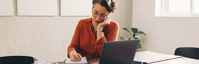 Woman writing in notebook in front of computer