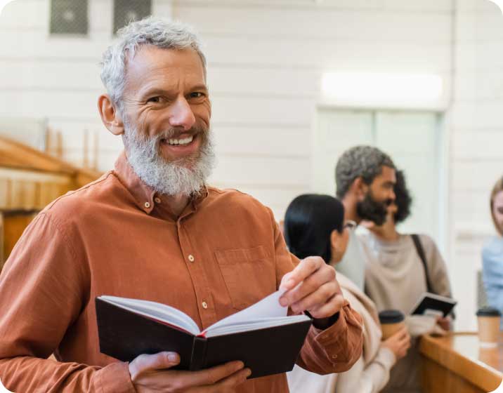 Man with book smiling and students in background