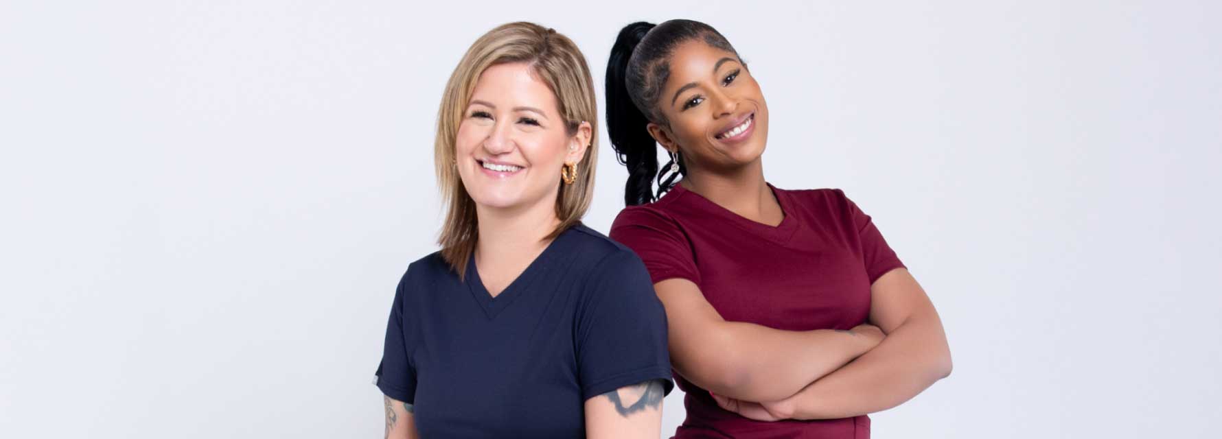 Two nurses wearing PNK Scrubs back to back posing